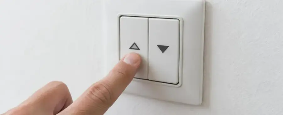 Main appuyant sur l'interrupteur à deux flèches d'un volet roulant électrique